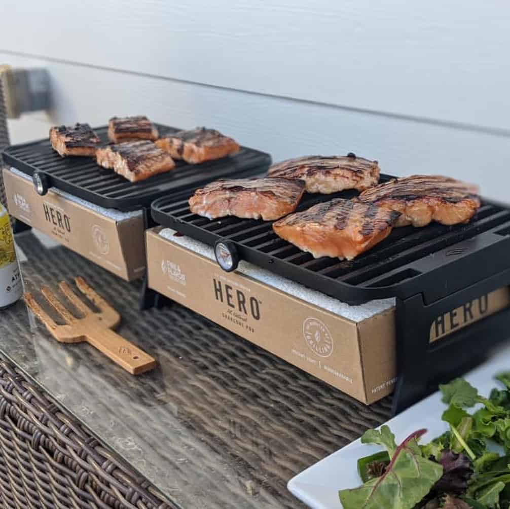 BBQ grills with grilled steaks and ribs on a wooden outdoor dining table, showcasing premium outdoor cooking and wood-fired grilling expertise by Cedar Works.